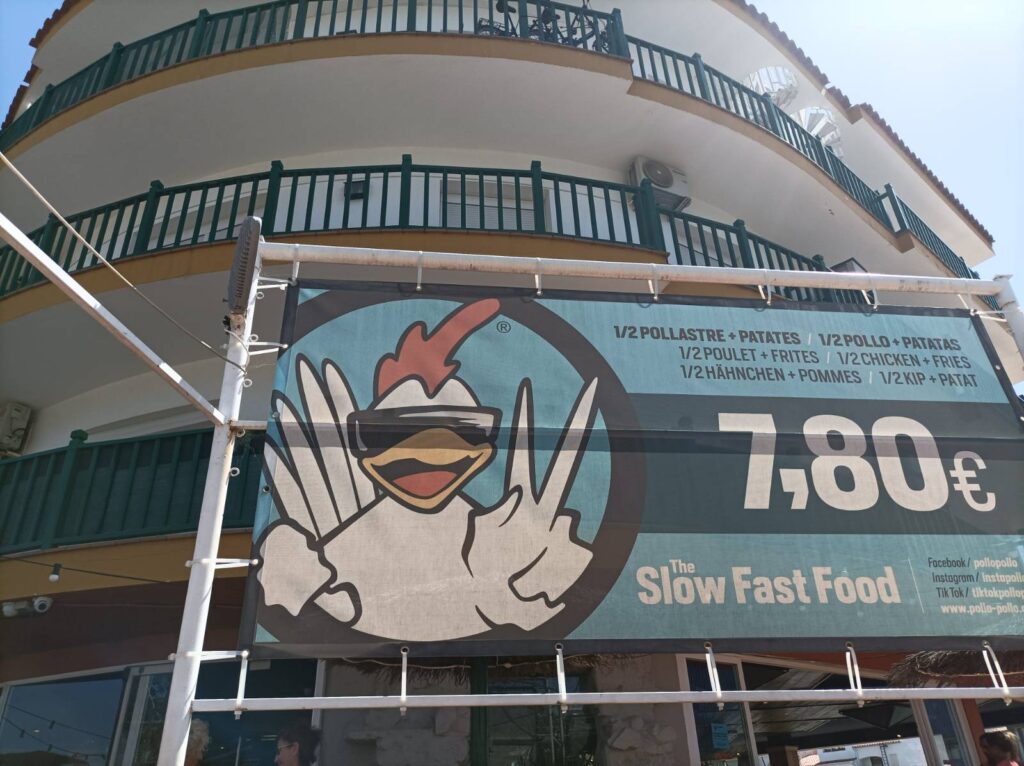 Autoría: Esteve Robleda i Sastre.Publicidad especista y cotidiana: un pollo sonríe, hace el signo de la victoria y anuncia el precio de pollos matados y troceados. La antropomorfización lo convierte en alegre consentidor de su propia explotación, invisibilizando la violencia —y legitimándola.